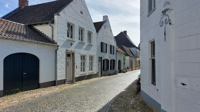 A narrow cobblestone street lined with white, gabled houses under a blue sky.