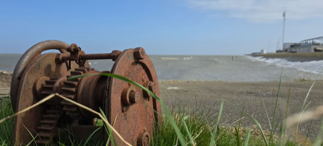 Rusty mechanical gears on grass with a beach and ocean in the background.