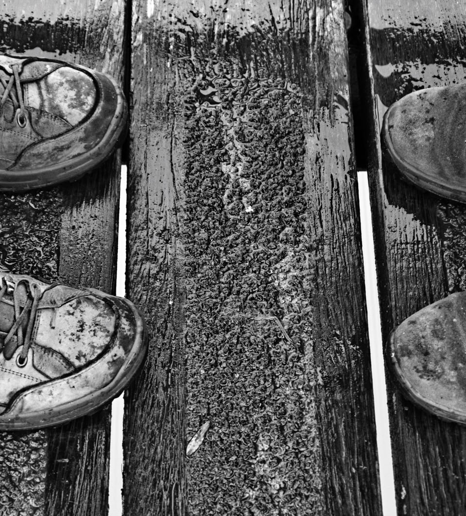 Two pairs of worn hiking boots facing each other on a wet wooden surface with metal strips.
