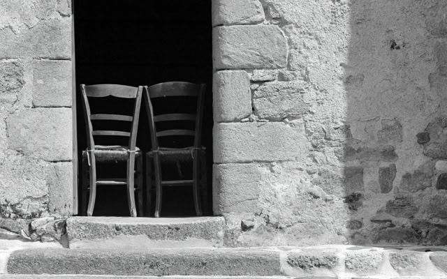 Two wooden chairs placed side by side in a doorway of a stone building. Church.