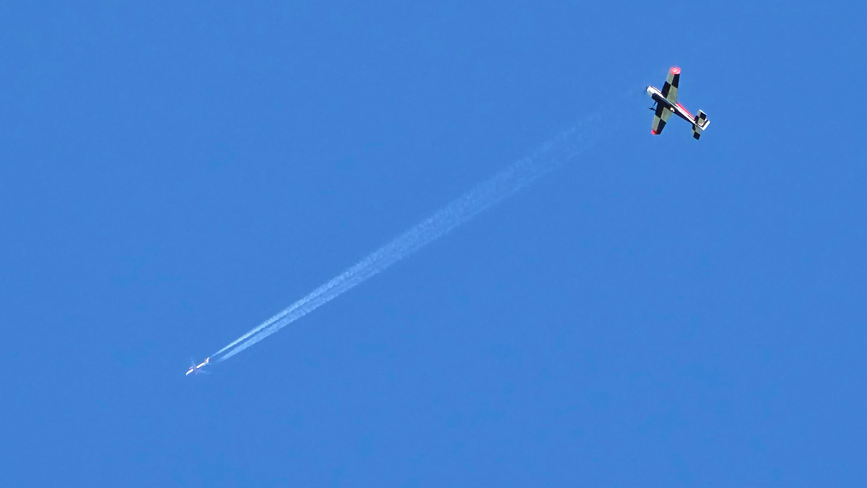 Airplane flying in a clear blue sky with a contrail behind it.