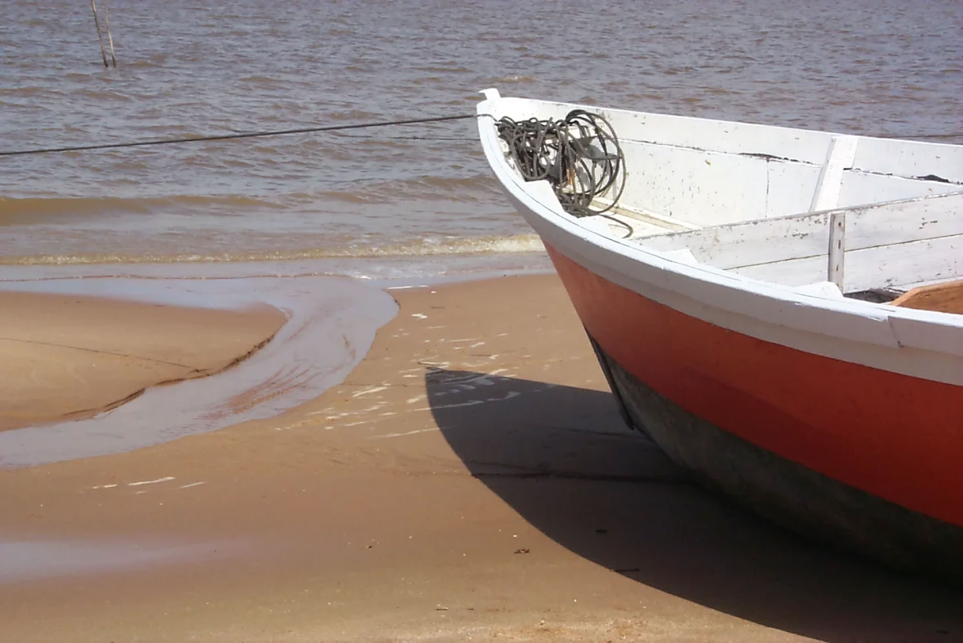 A small red and white boat on a sandy beach near the water's edge.