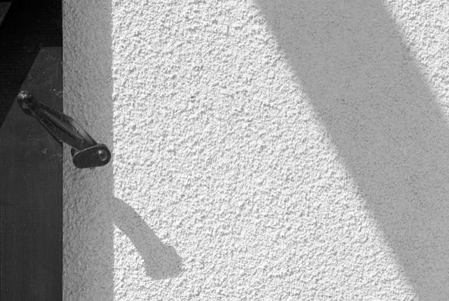 A textured white wall with a metal bracket casting a shadow.