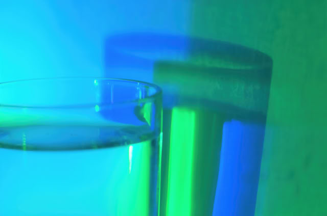 A glass of water with a blue and green light reflection on the surface and background.